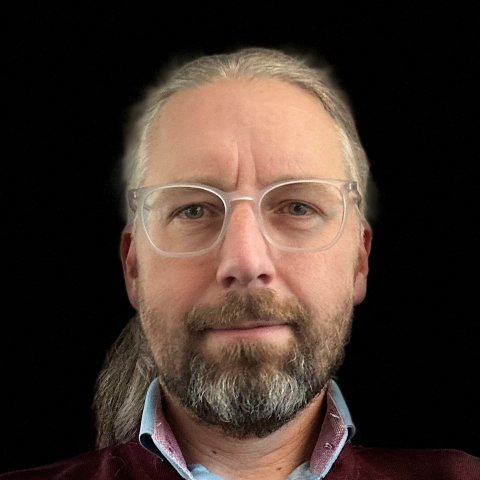 Mann mit langen grauen Haaren, Pferdeschwanz, Brille und Vollbart, lächelt